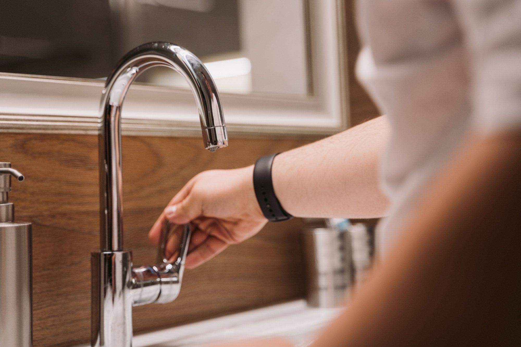 Mano abriendo la llave cromada de un lavabo de baño